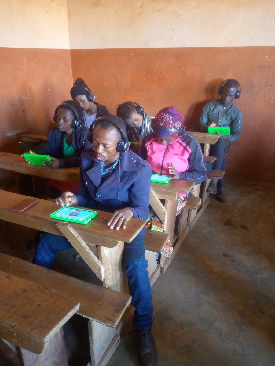 Adult learners wearing headphones using tablets at classroom desks