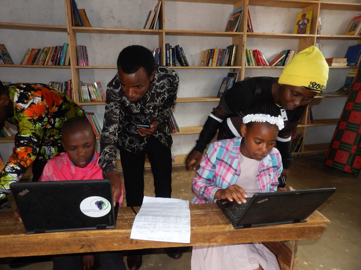 Mentors coaching two students on laptops in a library