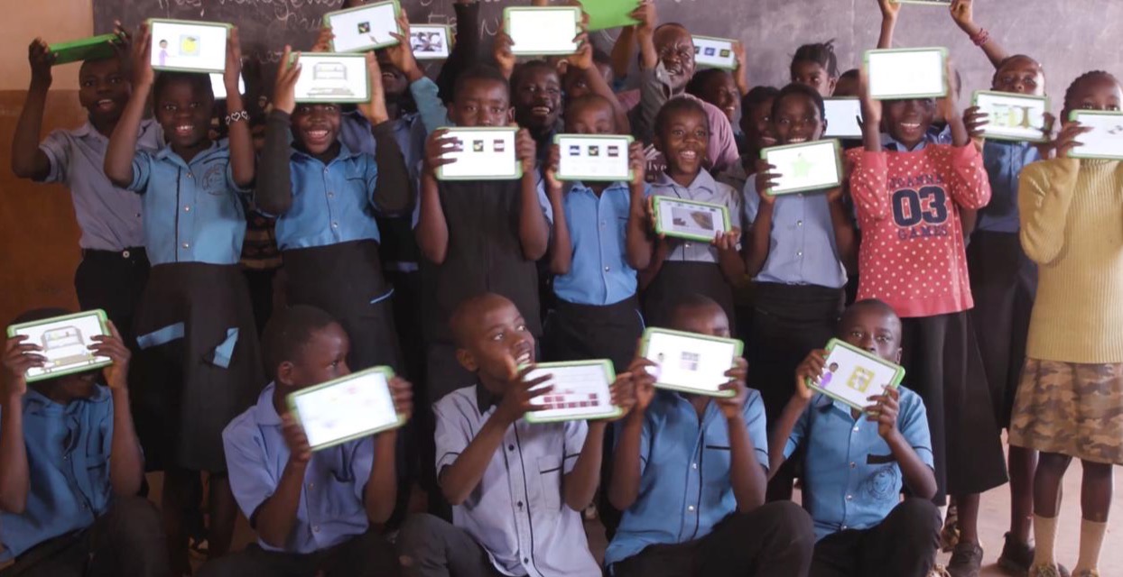 A classroom of smiling students holding up OneTab tablets